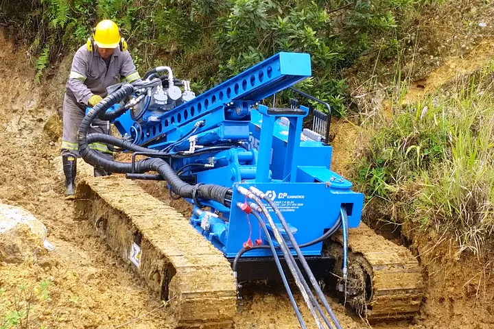 Operario manejando una perforadora sobre orugas en una ladera.